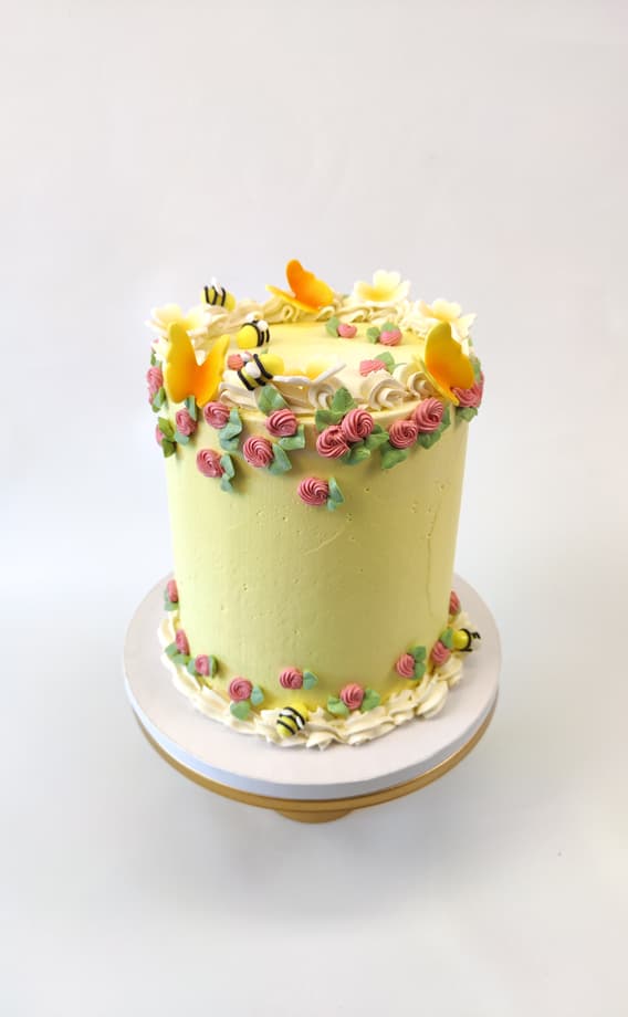 Käsintehty syntymäpäiväkakku, koristeltu keltaisilla kukilla ja suloisilla mehiläisillä.